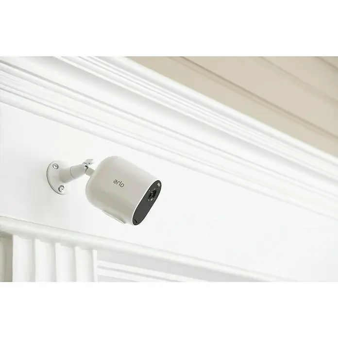 Arlo Überwachungskamera Essential 3er Set - 1.080 Pixel (Full HD), Erfassungswinkel: 130 °, Weiß, 3 Stk. - Eine weiße Arlo-Überwachungskamera ist an einer weißen Wand mit Zierleisten montiert. Die Kamera ist so positioniert, dass sie den Raum überwacht.