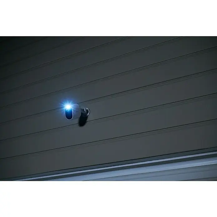 Arlo Überwachungskamera Essential 3er Set - 1.080 Pixel (Full HD), Erfassungswinkel: 130 °, Weiß, 3 Stk. - Eine moderne Überwachungskamera mit Nachtsicht ist an einer Wand montiert und leuchtet hell, um Sicherheit zu gewährleisten.