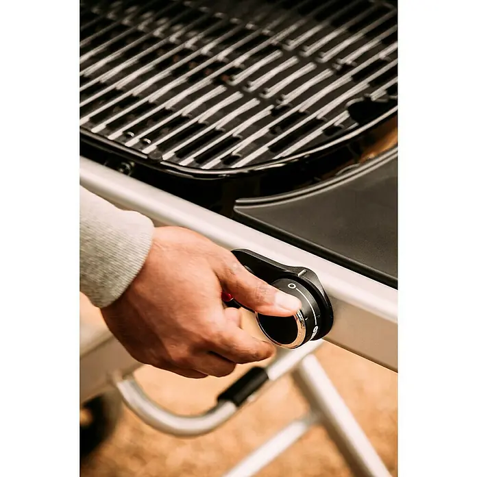 Weber Barbacoa de gas Traveler - Superficie de la parrilla (An x Pr): 64 x 35 cm, 3,8 kW, Número de quemadores: 1 - Primer plano de un hombre ajustando la perilla de control en una parrilla para ajustar la temperatura para una experiencia de parrilla perfecta.