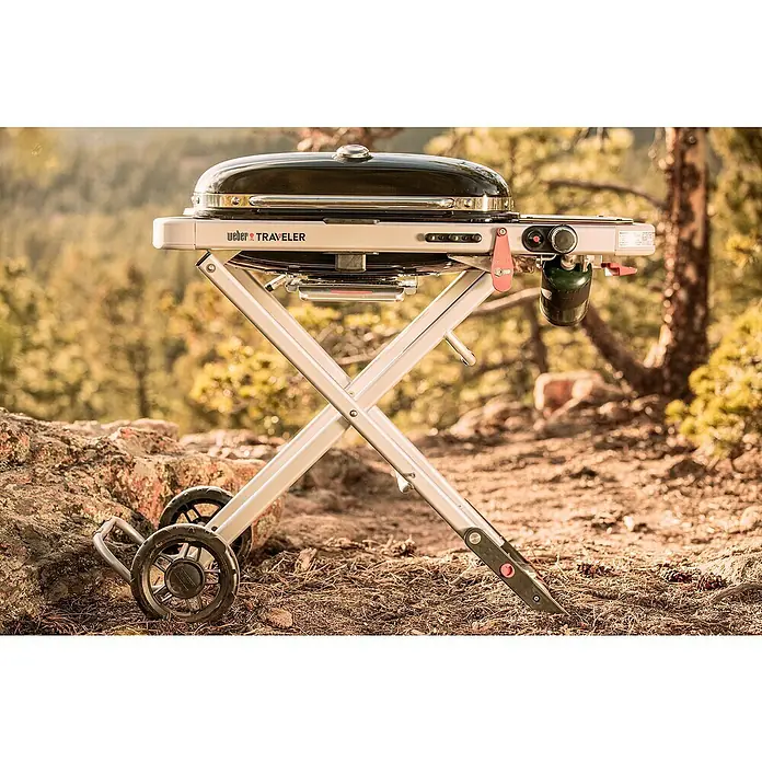 Weber Barbacoa de gas Traveler - Superficie de la parrilla (An x Pr): 64 x 35 cm, 3,8 kW, Número de quemadores: 1 - Imagen de una parrilla Weber Traveler al aire libre, que destaca su portabilidad y diseño para asar a la parrilla sobre la marcha.