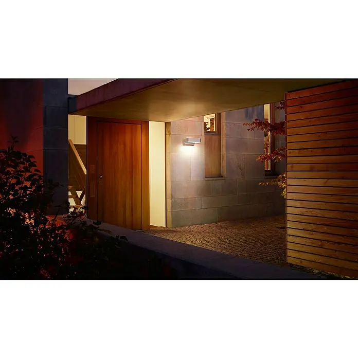 Steinel Aplique exterior LED con sensor L 800 SC - L x An x Al: 14,6 x 23 x 8,8 cm - Vista exterior iluminada de una casa moderna que muestra detalles de madera y una puerta acogedora que revela una escalera interior.