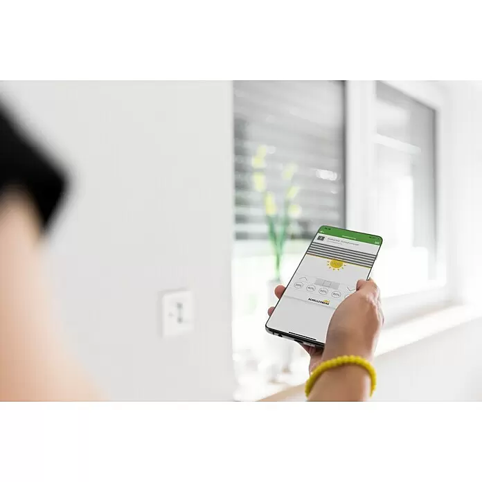 Schellenberg Smart Home Interruptor de recepción por radio - 80 x 80 x 40 mm, Blanco, Montaje enrasado - Mano sostiene smartphone con app para controlar persianas inteligentes al 40%, con persianas parcialmente bajadas en el fondo.