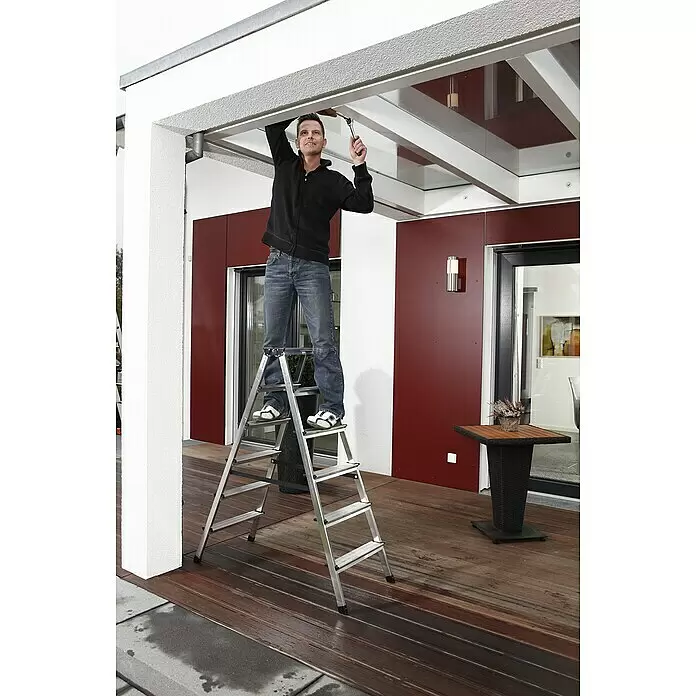 Krause Monto Doppel-Stehleiter Dopplo - Arbeitshöhe: 2,85 m, Anzahl Tritte: 12 Stk., Belastbarkeit: 150 kg, Aluminium - Silberne Aluminium-Klappleiter, die einen Mann bei der Arbeit an einer transparenten Überdachung stützt. Ideal für erhöhte Arbeiten.
