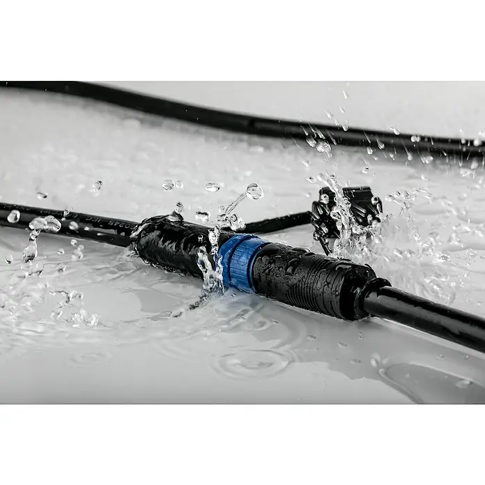 Paulmann Plug & Shine Bodeneinbauleuchte Lichtleiste8 W, Warmweiß, IP67, L x B x H: 90 x 5,4 x 4,5 cm - Detailaufnahme eines wasserdichten Steckverbinders mit blauen Elementen und spritzendem Wasser, ideal für Außenanwendungen.