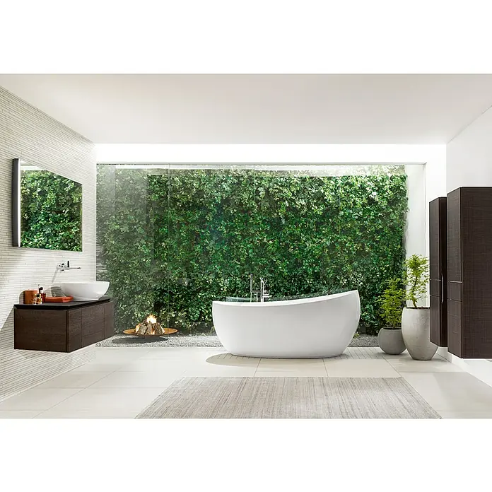 Villeroy & Boch Aveo New Generation Freistehende Badewanne - L x B: 190 x 95 cm, Quaryl, Weiß, Mit Ab-und Überlaufgarnitur und Wassereinlauf - Helles Badezimmer mit weißer Badewanne im Vordergrund, ergänzt durch einen dunklen Waschtisch und einen begrünten Hintergrund für eine entspannende Atmosphäre.