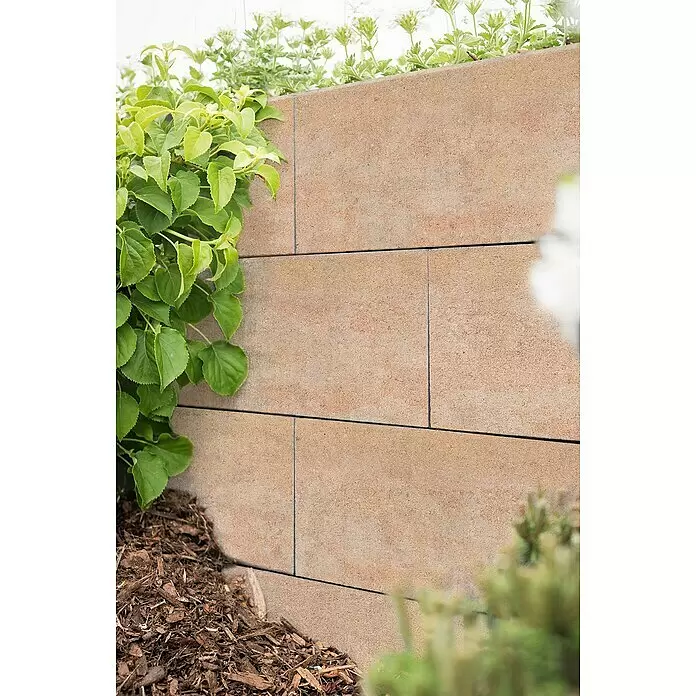 Diephaus Schalungsstein Cary - 50 x 24 x 25 cm, Sandstein, Beton - Strukturierte hellbraune Stützmauersteine bilden eine Gartenbegrenzung mit grünen Pflanzen.