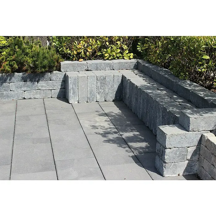 Diephaus Terrassenplatte Portland - 60 x 40 x 4 cm, Quarzit, Beton - Graue Steinblöcke bilden eine stilvolle Terrassenbegrenzung und eine niedrige Mauer, die das Grün elegant von der gepflasterten Fläche trennt.
