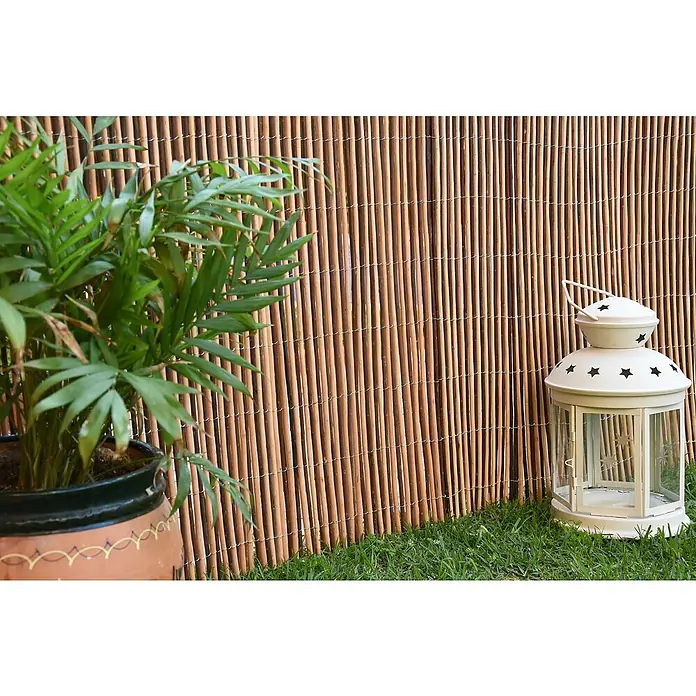 Faura Ocultación de mimbre Bicolor - L x Al: 3 x 2 m, Mimbre, Marrón - Primer plano de una linterna de jardín decorativa con motivos de estrellas, una planta verde en maceta y una valla de bambú al fondo.