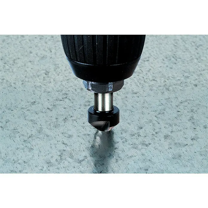 Wolfcraft Avellanador cónico - Diámetro: 12 mm, Acero, Varilla redonda - Primer plano de un avellanador con un manguito en un taladro, excavando en una superficie metálica galvanizada.