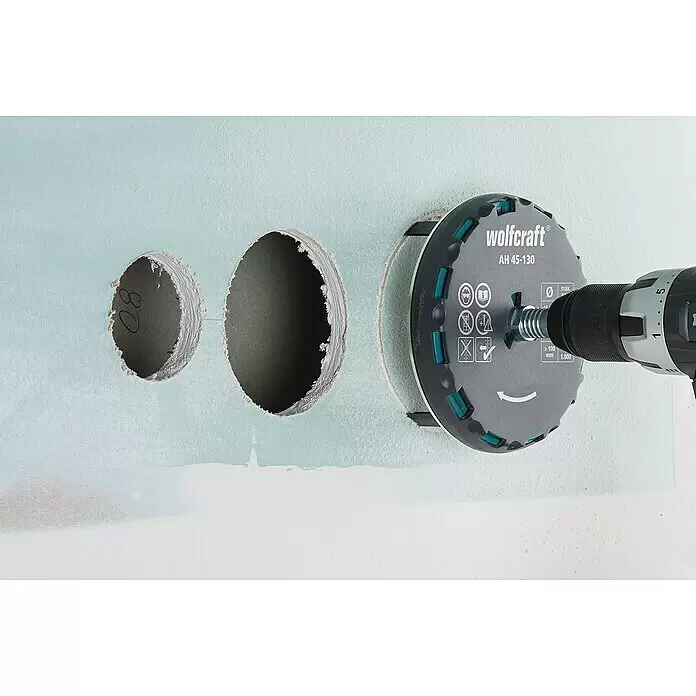 Wolfcraft Lochsäge verstellbar - Arbeitsdurchmesser: 45 mm - 90 mm, Schnitttiefe: 30 mm - Graue und türkisfarbene Wolfcraft Lochsäge an Bohrmaschine schneidet ein Loch in hellblaue Trockenbauwand. Zwei weitere Löcher sind sichtbar.