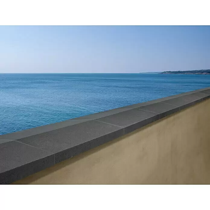 Mauerabdeckplatte Satteldach - Anthrazit, 50 x 30 cm, Beton - Dunkelgrauer Betonabdeckstein schützt eine hellbraune Mauer mit Blick auf das blaue Meer und die Küste.