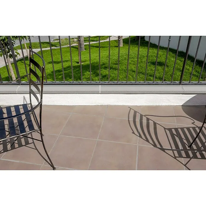 Mauerabdeckplatte - 100 x 30 cm, Naturgrau, Beton - Blick von einem Balkon mit einem schwarzen Metallstuhl auf Fliesen und einen Ausblick auf einen grünen Rasen und Bäume.
