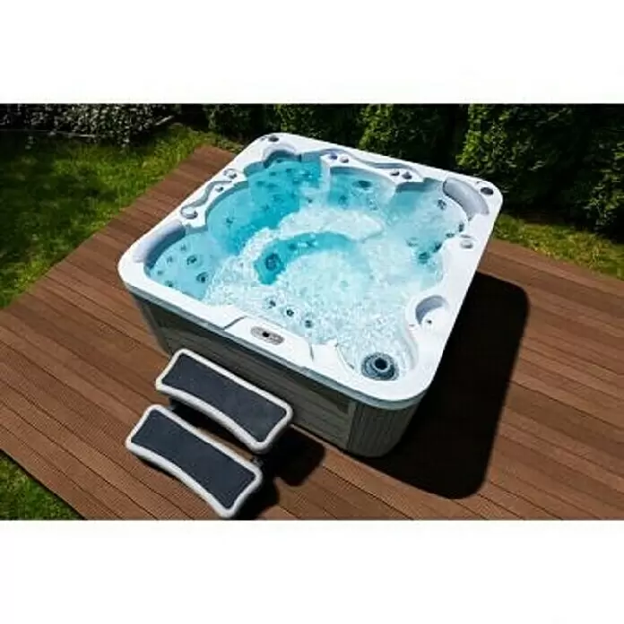 Camargue Außen-Whirlpool Harmony - 200 x 200 x 87 cm, Grau/Weiß, Max. Personenzahl: 6 - Weißer Outdoor-Whirlpool mit sprudelndem blauem Wasser auf einer Holzterrasse, begleitet von zwei hellgrauen Stufen.