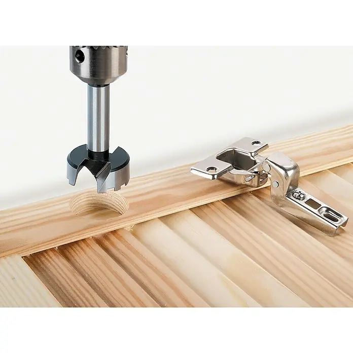 Wolfcraft Forstnerbohrer-Set5 -tlg., Durchmesser Schaft: 10 mm - Forstnerbohrer beim Herstellen eines Lochs für ein Möbelscharnier, das neben dem bearbeiteten Holzstück liegt.