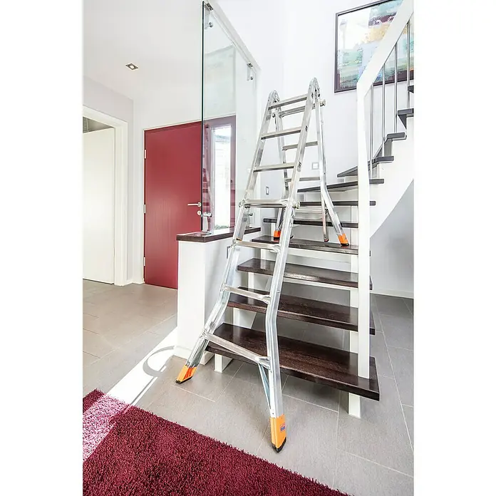 Krause Monto Teleskopleiter TeleMatic - Anzahl Tritte: 16 Stk., Arbeitshöhe: 5 m, Aluminium - Eine silberne Mehrzweckleiter von Krause lehnt an einer Treppe im Innenbereich, ideal für Renovierungsarbeiten.