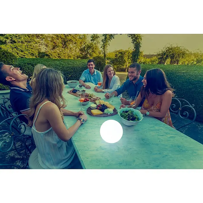 New Garden Solar-Dekoleuchte Buly - Durchmesser: 20 cm, IP65 - Ein weißer, runder Tischlampe, die eine fröhliche Gruppe am Tisch beleuchtet, während sie eine Mahlzeit im Freien genießen.