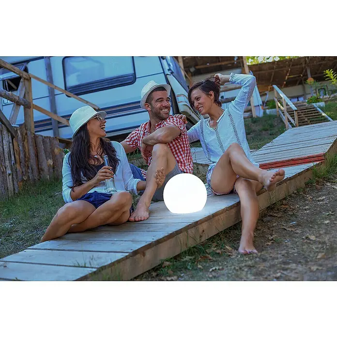 New Garden Solar-Dekoleuchte Buly - Durchmesser: 30 cm, IP65 - Drei Freunde sitzen mit einem beleuchteten Globus auf einer Holzterrasse vor einem Wohnwagen und lachen.