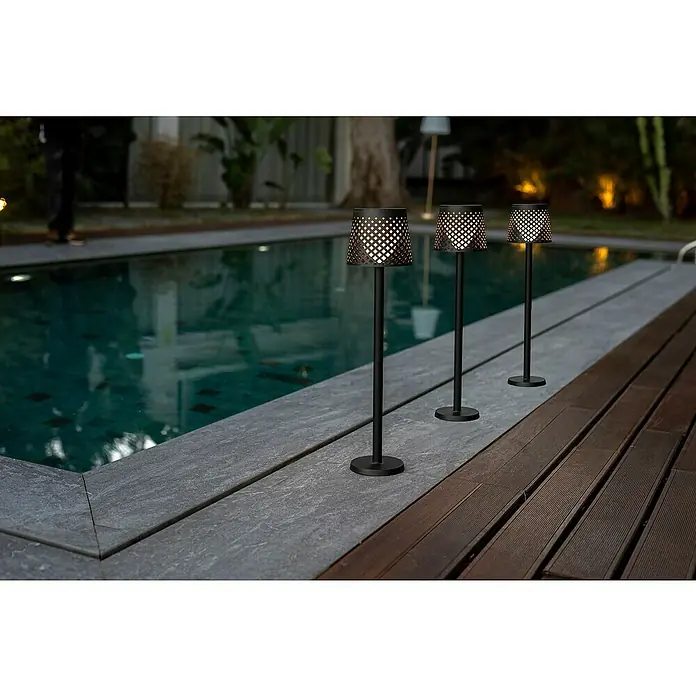New Garden Lámpara decorativa solar Greta - 0,5 W, Negro, IP65 - Tres elegantes lámparas de exterior con diseño perforado decorativo junto a una piscina, creando un ambiente cálido.
