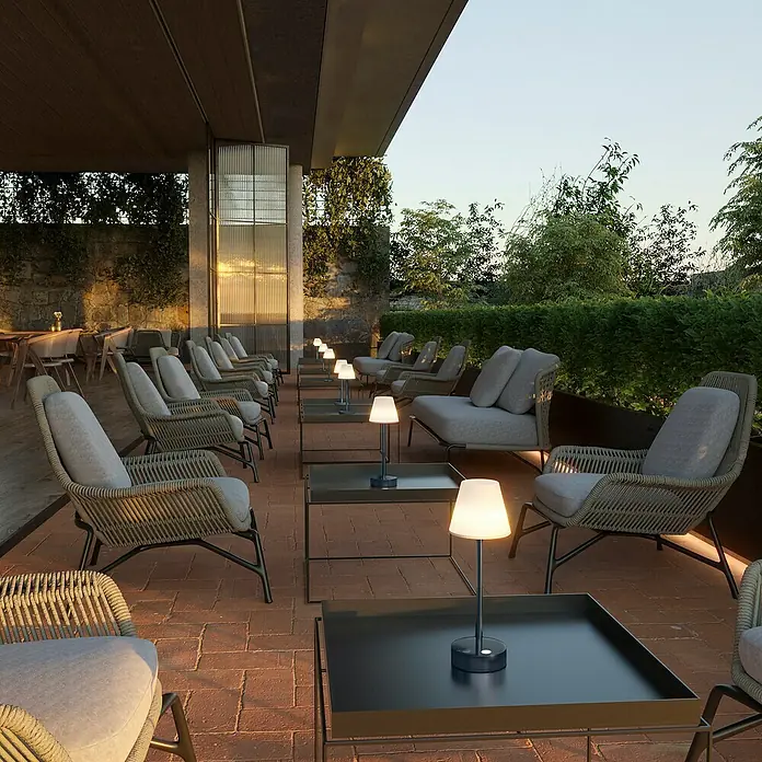 New Garden Akku-Tischleuchte Lola Slim - Anthrazit, Warmweiß, 2 W, IP44 - Elegante Outdoor-Szene mit bequemen Korbsesseln und stilvollen Tischlampen auf einem Ziegelboden. Perfekt für entspannte Abende im Freien.
