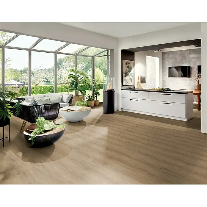 b!design Vinylboden Rigid Maxi - Columbia Eiche, Landhausdiele, 1.220 x 228 x 4,8 mm - Elegantes Interieur mit Fokus auf dem hellbraunen Holzboden, der Wärme und Natürlichkeit in den Raum bringt. Moderne Möbel und Pflanzen ergänzen das Ambiente.