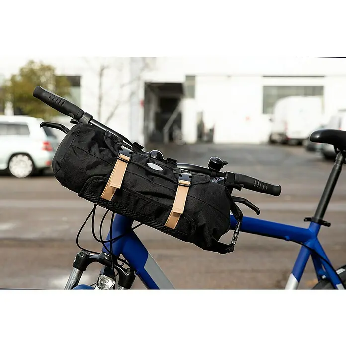 Lenkertasche - Volumen: 10 l, Schwarz - Nahaufnahme einer schwarzen Fahrradlenkertasche mit hellbraunen Riemen an einem blauen Fahrrad vor einem Gebäude.