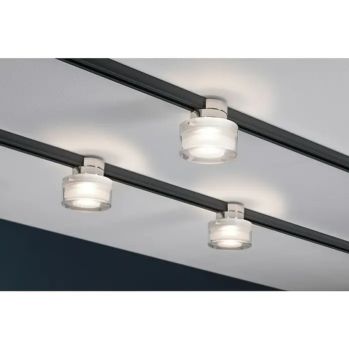 Paulmann URail LED-Spot Topa - 5,2 W, Chrom matt/Transparent/Satin, L x B x H: 73 x 80 x 80 mm - Nahaufnahme von drei silbernen Schienenstrahlern mit zylindrischen Glasschirmen, die an einer Decke montiert sind und helles Licht abgeben.