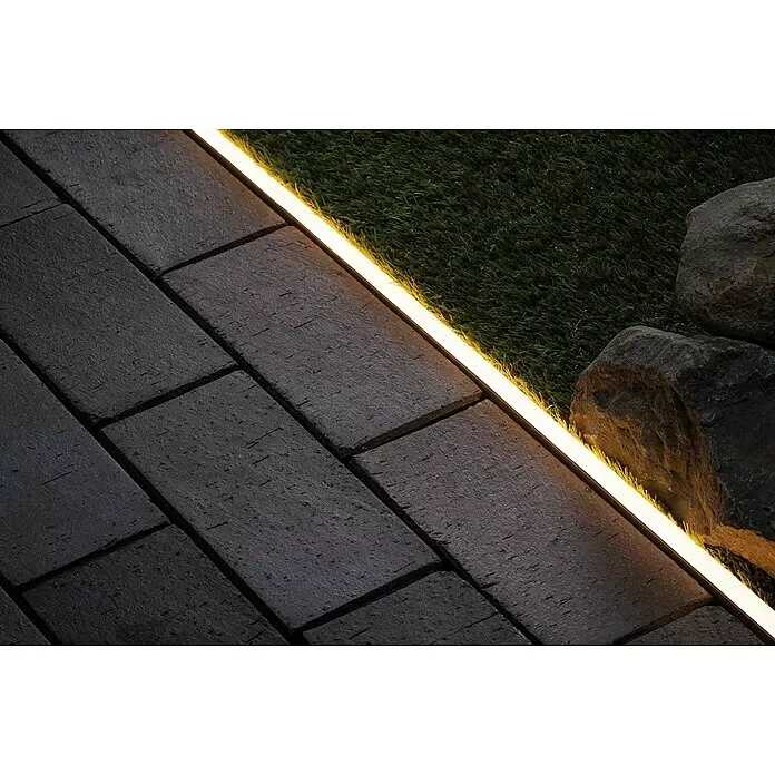 Paulmann Plug & Shine Montageschiene für Neon Stripe - Länge: 1 m - Warme LED-Lichtleiste beleuchtet einen dunklen Ziegelweg neben Kunstrasen und Felsen.
