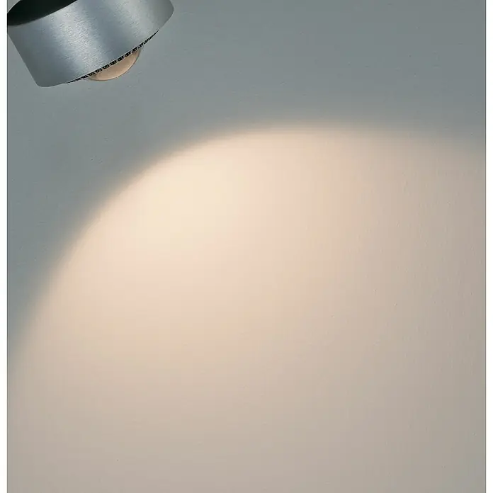 Paulmann URail Foco LED para riel Aldan - 9 W, Cromado mate, L x An x Al: 9,8 x 9,8 x 17 cm - Primer plano de una lámpara plateada moderna que proyecta una luz cálida sobre una pared blanca. Iluminación elegante para un hogar moderno.