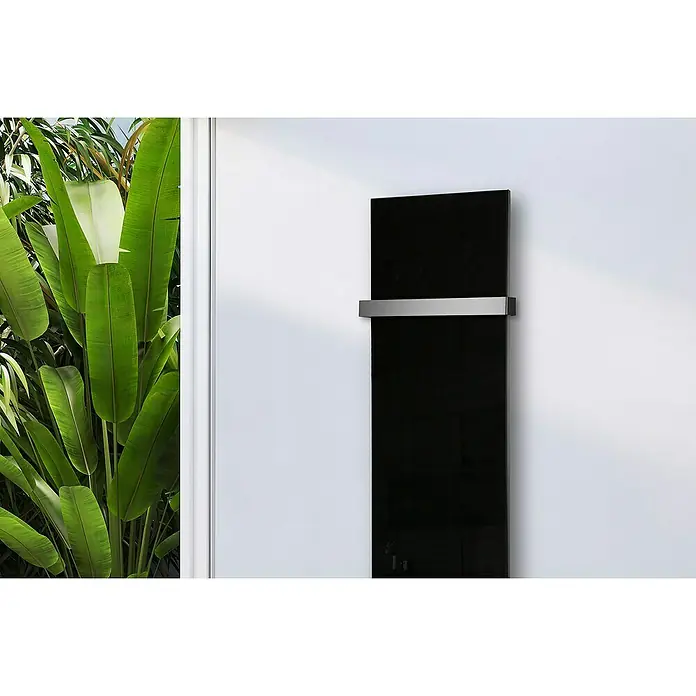 Szagato Designheizkörper Montevideo - B x H: 470 x 1.800 mm, Schwarz, Mit 1 Handtuchhalter (50 mm) - Ein hochformatiger, schwarzer Heizkörper mit einem silberfarbenen Handtuchhalter an einer weißen Wand, neben üppigen grünen Pflanzen.