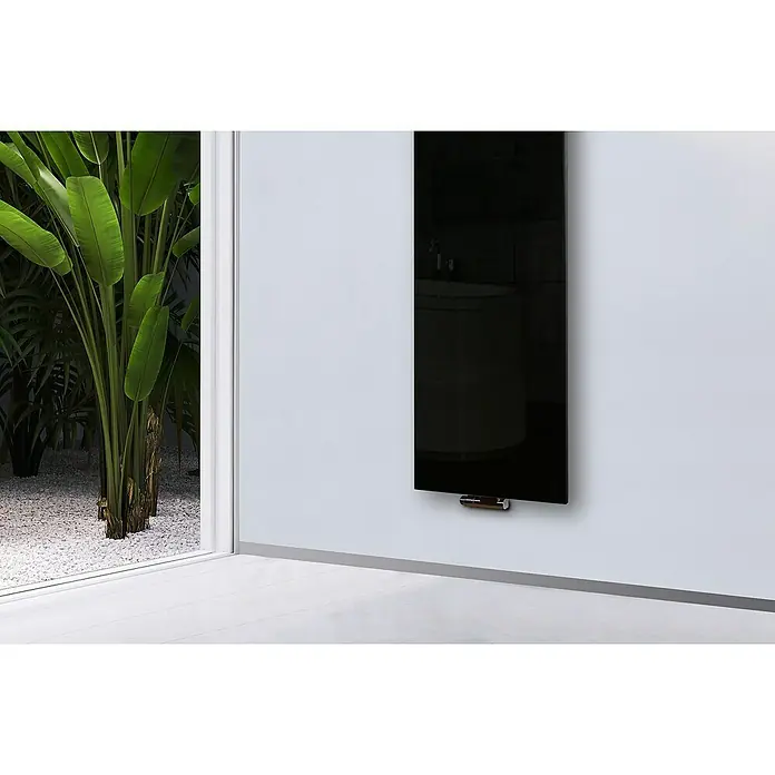 Szagato Designheizkörper Montevideo - B x H: 470 x 1.800 mm, Schwarz, Ohne Handtuchhalter - Dieses Bild zeigt einen eleganten schwarzen Heizkörper an einer weißen Wand, mit Pflanzen und Kies im Hintergrund.