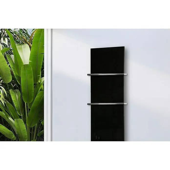 Szagato Designheizkörper Montevideo - B x H: 470 x 1.800 mm, Schwarz, Mit 2 Handtuchhalter (15 mm) - Ein hochformatiger, schwarzer Heizkörper mit zwei chromfarbenen Handtuchhaltern schmückt eine weiße Wand, neben üppigem Grün.