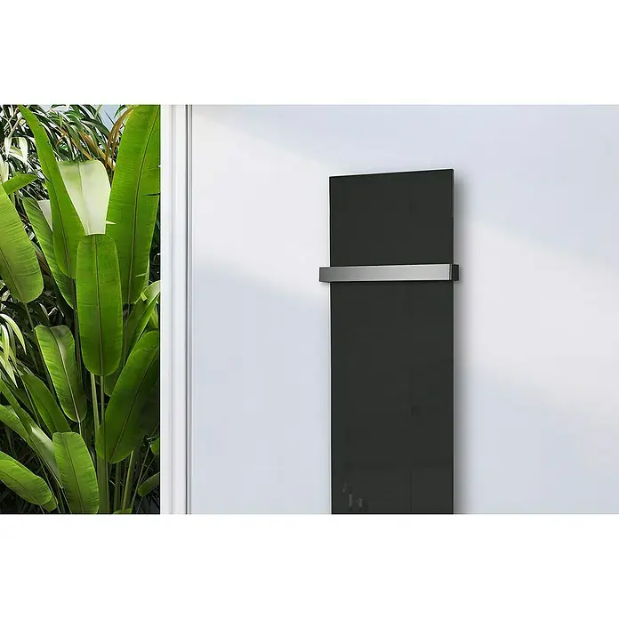 Szagato Designheizkörper Montevideo - B x H: 470 x 1.800 mm, Grau, Silber, Mit 1 Handtuchhalter (50 mm) - Ein moderner, schwarzer Heizkörper mit einem schlanken, silbernen Handtuchhalter an einer weißen Wand neben üppigen Grünpflanzen.