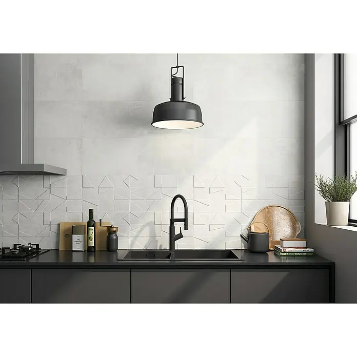 Revestimiento de pared Madox - 30 x 90 cm, Blanco, Mate, Rectificado - Moderna cocina con encimera oscura, fregadero y protector contra salpicaduras con estampado abstracto, iluminada por lámpara colgante.