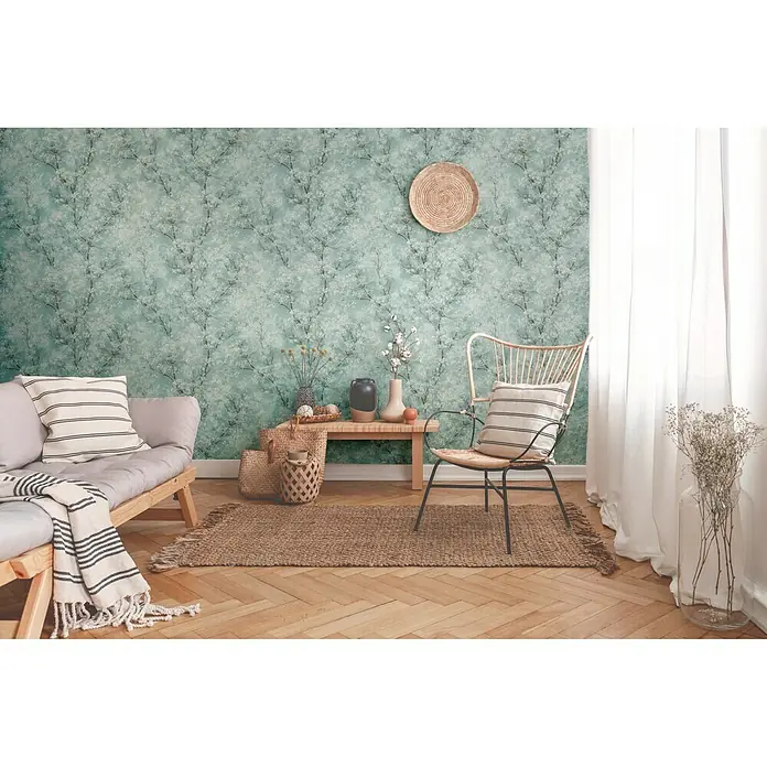 A.S. Création New Walls Vliestapete Bäume - Blau/Grün, Floral, 10,05 x 0,53 m - Zimmeransicht mit Couch, Stuhl, Teppich und Dekoration vor einer grünen gemusterten Wand.