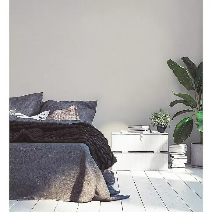 A.S. Création Industrial Vliestapete - Creme, Uni, 10,05 x 0,53 m - Ein Bett mit grauer Leinen- und dunkler Grobstrickbettwäsche in einem hellen, minimalistischen Schlafzimmer.