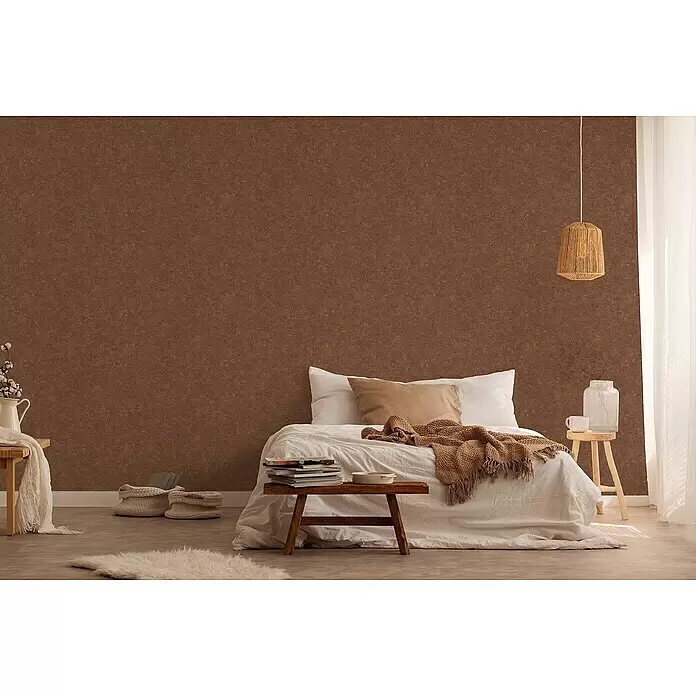 A.S. Création Industrial Vliestapete - Braun, Uni, 10,05 x 0,53 m - Texturierte braune Wand in einem Schlafzimmer mit Bett, weißer Bettwäsche und Holzelementen.
