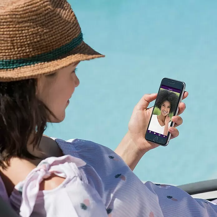 Philips WelcomeEye Videoportero Connect 2 - Plateado - Una persona con sombrero de paja mira un smartphone junto a una piscina. La pantalla muestra a una mujer sonriente.