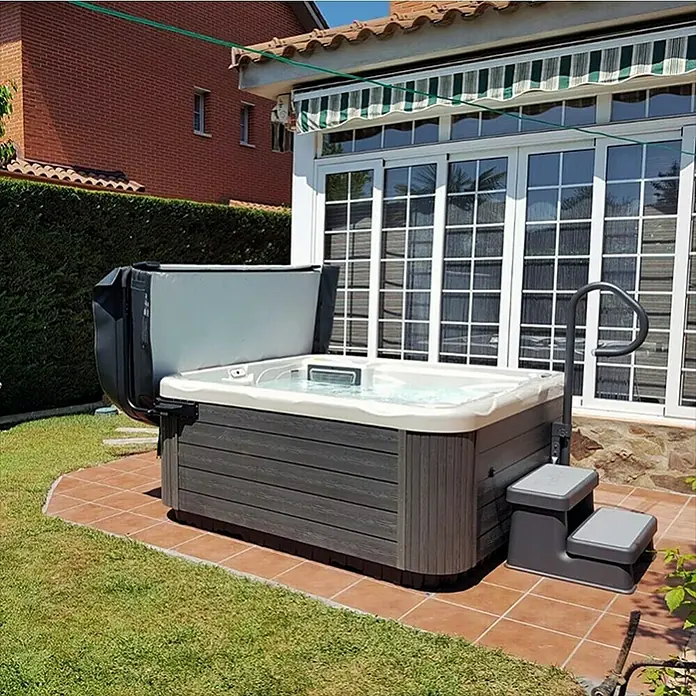 Camargue Außen-Whirlpool Spirit - 200 x 200 x 89 cm, Grau/Weiß, Max. Personenzahl: 5 - Das Bild zeigt einen modernen Whirlpool im Garten mit geöffnetem Deckel, Treppe und Haltegriff. Der Pool steht auf Fliesen neben einer grünen Rasenfläche.