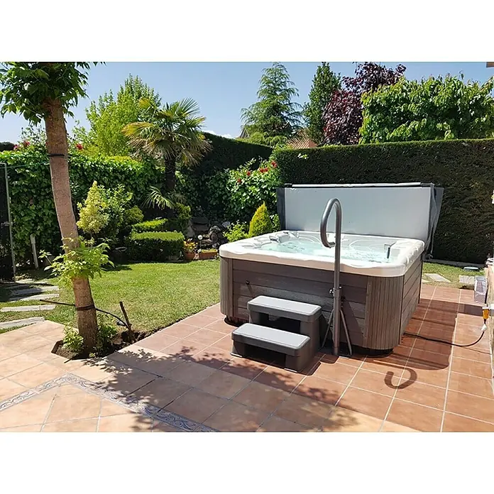 Camargue Außen-Whirlpool Spirit - 200 x 200 x 89 cm, Grau/Weiß, Max. Personenzahl: 5 - Nahaufnahme eines Whirlpools im Garten mit Treppe, Abdeckung und Handlauf für einfachen Einstieg und Entspannung im Freien.
