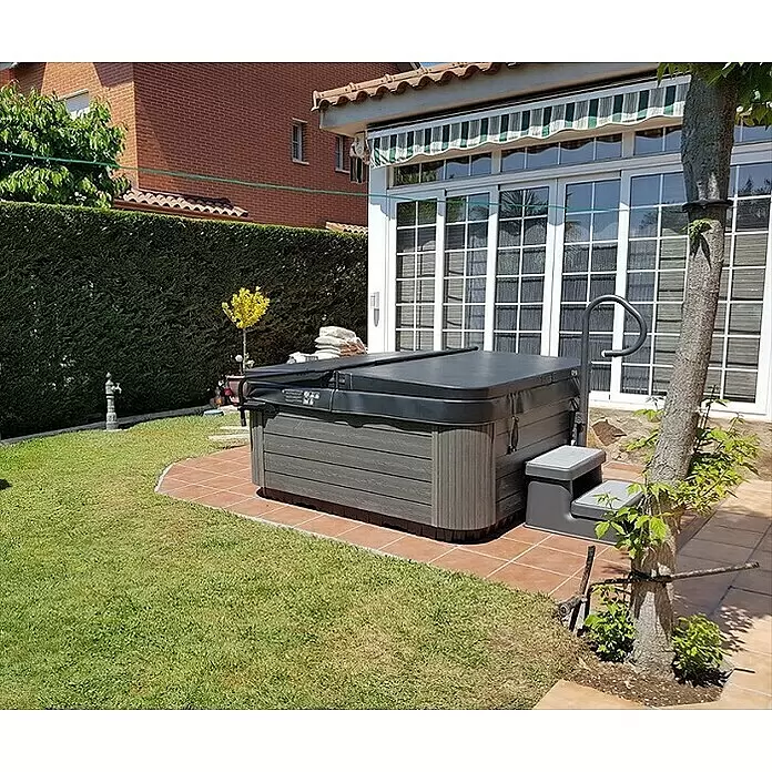 Camargue Außen-Whirlpool Spirit - 200 x 200 x 89 cm, Grau/Weiß, Max. Personenzahl: 5 - Dunkelgrauer Whirlpool mit Stufen und Haltegriff auf einer Terrasse, mit schwarzer Abdeckung im Garten.