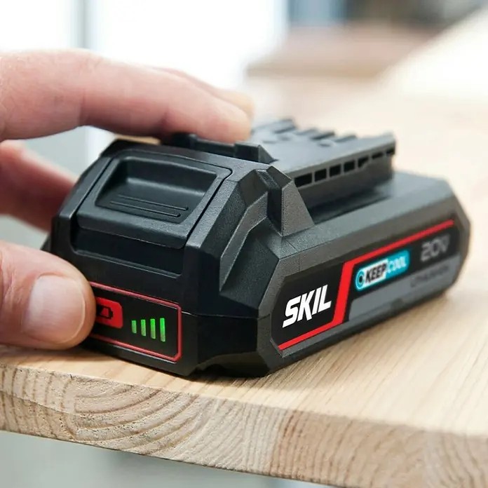Skil PWRCore 20V Akku 3102 AA - 20 V, 2,5 Ah - Nahaufnahme eines Skil 20V Lithium Akkus mit Batteriestandsanzeige auf einem Holztisch. Der Akku ist schwarz mit roten Akzenten.