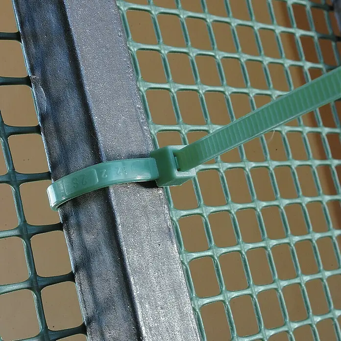 Tenax Set de bridas para cables - Largo: 29 cm, 50 ud., Verde - Primer plano de una brida de cable verde que asegura una malla a un marco metálico. La brida garantiza un agarre seguro en la rejilla.