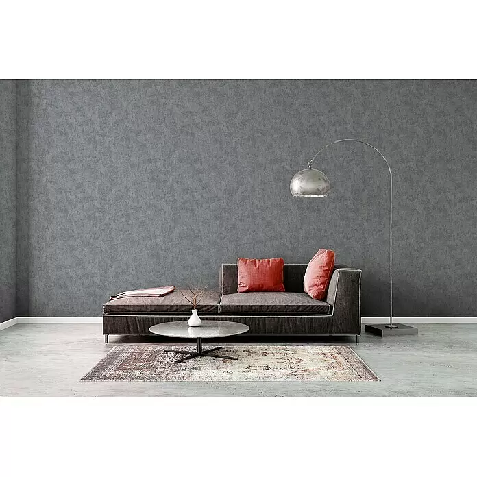 A.S. Création Blooming Vliestapete Betonoptik - Grau, Uni, 10,05 x 0,53 m - Dunkelgraues Récamière-Sofa mit roten Kissen in einem modernen Wohnzimmer, neben Couchtisch und Stehlampe.