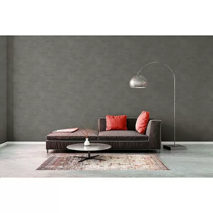 A.S. Création Elements Vliestapete - Betongrau, Betonoptik, 10,05 x 0,53 m - Dunkelgraues Chaiselongue-Sofa mit leuchtend roten Kissen, in minimalistischem Wohnzimmer-Stil.