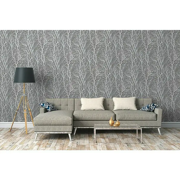 A.S. Création New Life Vliestapete Bäume - Grau/Silber, Floral, 10,05 x 0,53 m - Wohnzimmer mit grauer Couch, Couchtisch und Stehlampe vor einer silbernen Baumtapete, die ein modernes und stilvolles Ambiente schafft.