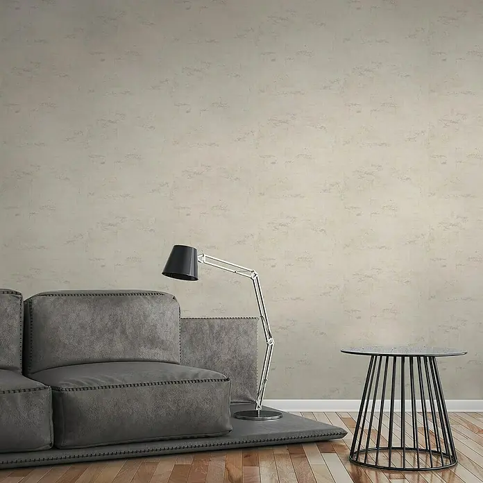 A.S. Création Elements Vliestapete - Beige, Betonoptik, 10,05 x 0,53 m - Ein modernes Wohnzimmer mit einem grauen Sofa, einer Stehlampe und einem Beistelltisch auf einem Holzboden. Die Wand hat eine dezente Textur.
