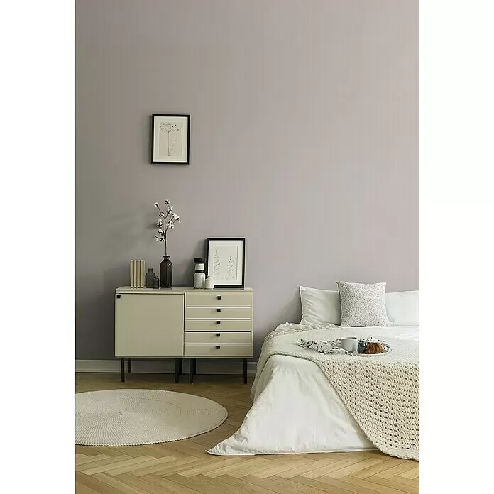 A.S. Création New Life Vliestapete - Grau, Uni, 10,05 x 0,53 m - Schlafzimmer mit einer hellbeigen Kommode, einem Bett mit weißer Bettwäsche und einem cremefarbenen Stricküberwurf sowie einem runden Teppich.