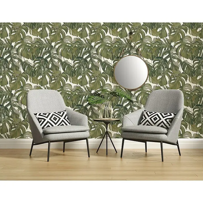 A.S. Création Michalsky Vliestapete - Grün, Floral, 10,05 x 0,53 m - Zwei graue Sessel mit Kissen vor einer Wand mit Monstera-Blättern und einem runden Spiegel. Das Ensemble strahlt moderne Eleganz aus.