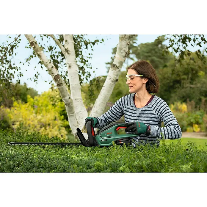 Bosch Power for All 18V Akku-Heckenschere UniversalHedgeCut 18V-55 - 18 V, Li-Ionen, 1 Akku, Schnittlänge: 50 cm - Frau schneidet mit einer Bosch Akku-Heckenschere eine Hecke. Die kabellose Heckenschere ist ein praktisches Gartengerät für den Heckenschnitt.