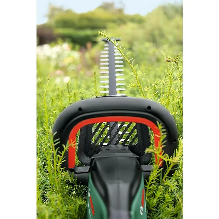 Bosch Power for All 18V Akku-Heckenschere UniversalHedgeCut 18V-55 - 18 V, Li-Ionen, 1 Akku, Schnittlänge: 50 cm - Detailaufnahme einer Bosch Heckenschere, die in dichtem, grünen Gras steht, mit Fokus auf die scharfen Schneideblätter und den ergonomischen Griff.